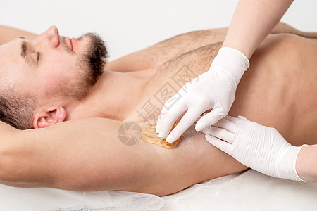 美容学专家在男性膝盖上施用蜡糊脱毛头发工作室腋窝水疗身体沙龙医学卫生美容师图片