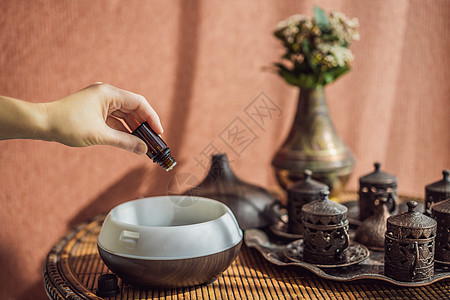 妇女在桌上的芳香扩散器中添加必要的石油瓶子桌子加湿器液体房间净化器治疗疗法蒸汽食谱图片
