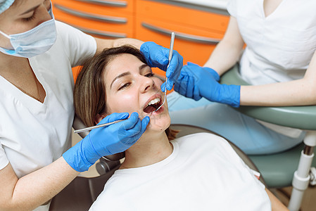 在牙医诊所接受治疗 女牙医和牙科诊所助理在牙科诊所用工具检查年轻女性图片