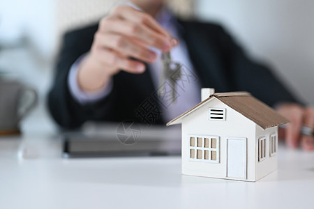 特写在白色桌上的视图房子模型和背景中拿着钥匙的商务人士 房地产 搬家或租房图片