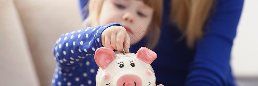 小女孩把硬币放进粉红小猪银行图片