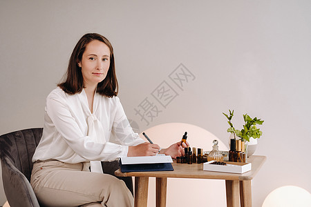 芳疗少女坐在自己的办公室里 手里拿着一瓶香油 正在写着什么 桌子上有精油护理美容女孩笔记本女性专家治疗女士身体药品图片