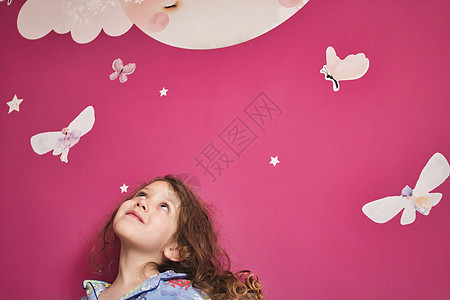 穿着睡衣的年轻可爱女孩 仰望着粉红色的墙壁 上面有露珠星星 月亮和仙女图片