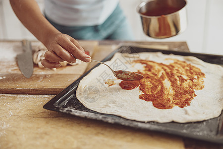一个女人的手把番茄酱倒在 烘烤盘上披萨上的表面图片
