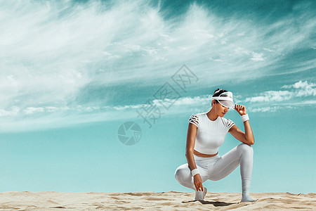 运动健美的年轻女运动员在沙漠训练后放松 在海岸的多云天 健康的生活方式和运动的概念 穿着白色运动服的女人日落女孩海滩天空灵活性生图片