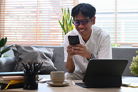 在家使用智能电话 与电脑平板电脑合作 微笑的男子自由职业者图片