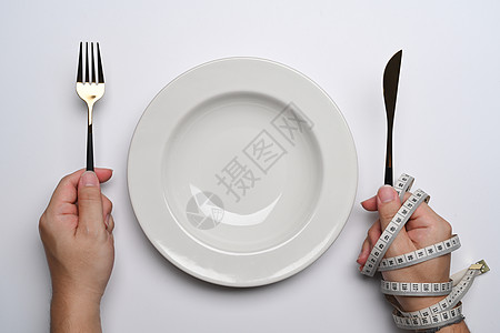 从上面看 妇女拿着刀和叉子在白色背景的空盘子附近 健康的生活方式概念图片