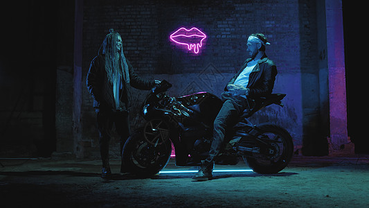 一个骑超运动摩托车的家伙 站在一个女孩对着粉红亮号说话骑士运输魔法摩托车库引擎速度皮革女士城市图片