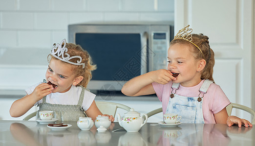 两个小女孩在家里举行公主茶话会 兄弟姐妹朋友在厨房的桌子上玩茶具和吃饼干时戴着头饰 姐妹相处和一起玩房子孩子们朋友们微笑女性青年图片