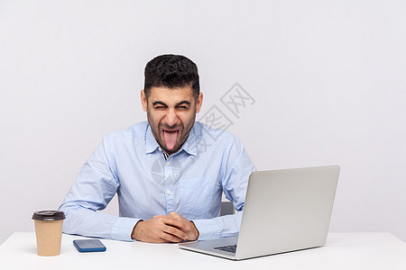 坐在办公室和工作着的情感男人电脑商业厌恶举止傻子自由职业者男性舌头笔记本职场图片