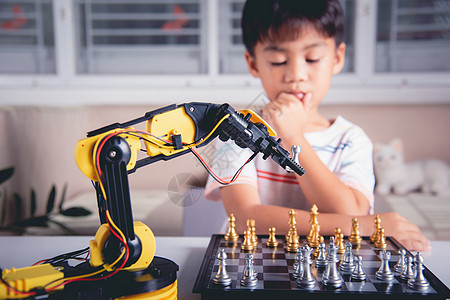 亚洲小男孩思考和等待机器人臂象棋游戏的亚洲男孩机械电子产品助手金属教育工程作坊孩子幼儿园学习图片