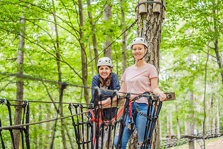 两名女性女孩在森林中的极端公路手推车滑索中滑行 在树上的登山扣安全连接到树顶绳索冒险公园 家庭周末儿童儿童活动概念头盔绳索风险运图片
