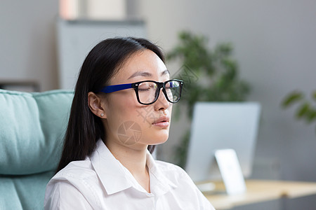 戴眼镜的女人工作休息 戴眼镜的亚洲女人坐在办公室里闭着眼睛歇息不眠背景