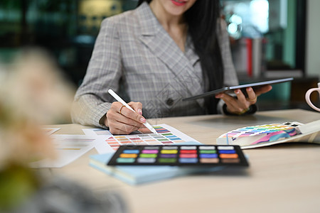 女青年室内设计师 在工作场所使用彩色手表和使用数字平板电脑工作;图片