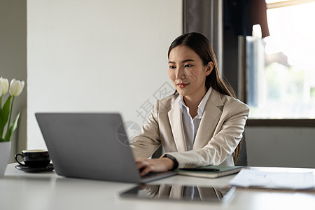 快乐的千禧一代亚洲女商务人士的肖像在家庭办公室在线使用笔记本电脑工作 微笑的年轻女雇员或工人在计算机上远距离咨询客户合作伙伴 技图片