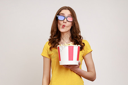 身戴3D眼镜和黄色短袖T恤的幼女 观看电影 拿着一桶爆米花 使鱼嘴唇脸红图片