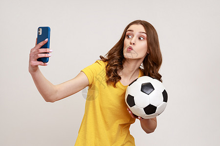 年轻有吸引力的少女身着黄色散装短袖T恤 自拍 带视频电话或用手边的球播放实况流图片