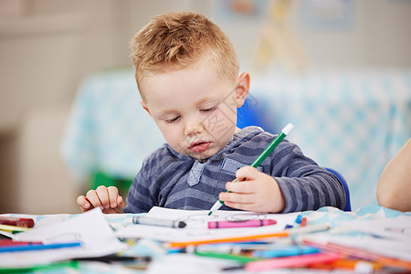 一个可爱的白人小男孩独自坐在桌旁 在学前班或幼儿园里画画 幼儿在教室里用彩色铅笔画画图片