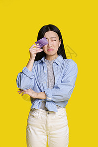 悲伤 不快乐的亚洲女孩用银行卡右眼遮住她 正要哭着说没钱 身穿蓝色衬衫的亚洲女孩 银行卡样机在黄色背景下被隔离 购物理念图片