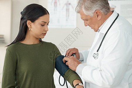 让我们看看是什么让你生病了 一位高级医生在诊所咨询期间站着检查病人的血压图片