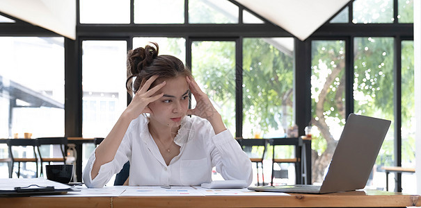一名疲劳妇女下班后 在木制工作台头顶着她的手 照片显示她累坏了挫折商务学生人士女性成人情感商业压力笔记本图片