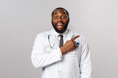 欢乐快乐 微笑的非洲美国医生邀请新客户到他的诊所 笑着和看着摄影机充满热情 指向右角 掌声 PAGHINT咨询隔离感染男人社交药图片