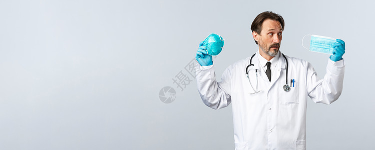 Covid19 预防病毒 医护人员和疫苗接种概念 优柔寡断的医生在医用口罩和呼吸器之间挑选 不知道穿什么 白色背景保险防护管子防图片