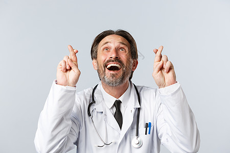 Covid19 预防病毒 医护人员和疫苗接种概念 乐观有希望的医生穿白大褂的特写 交叉手指祝你好运 抬头微笑 许愿医院擦洗感染病图片