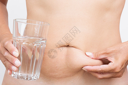 手抚摸肚子上的脂肪 手握杯纯水图片
