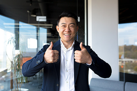 亚洲快乐的男人看着照相机 举起大拇指看好牌营销微笑手势职业管理人员拇指商业企业家商务办公室公司的高清图片素材