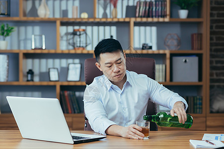 亚洲商务人士失败了 绝望的人喝烈酒 坐在桌子上晚坐的很晚男人孤独瓶子人士商务笔记本办公室酒精破产心理图片