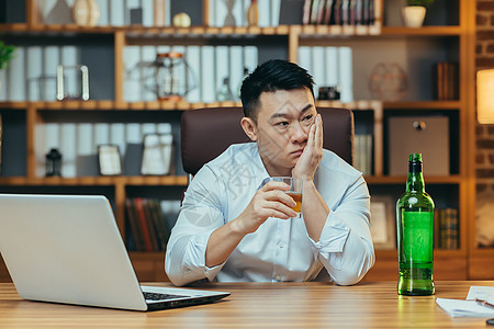 亚洲商务人士失败了 绝望的人喝烈酒 坐在桌子上晚坐的很晚酒精办公室失眠管理人员破产人士职场压力电脑玻璃图片