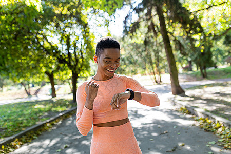 女运动员清晨在公园跑步 看健身手镯 欢欣鼓舞运动运动装成人智能阳光训练慢跑者福利时间女性图片