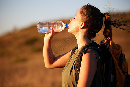 您不会厌倦远足 但会感到口渴 外出远足时喝水的年轻女子图片