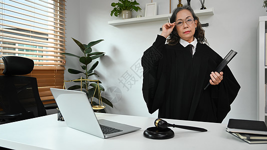 正面成熟的女法官 律师或身着长袍制服的律师站在她的私人办公室 法律和正义概念图片