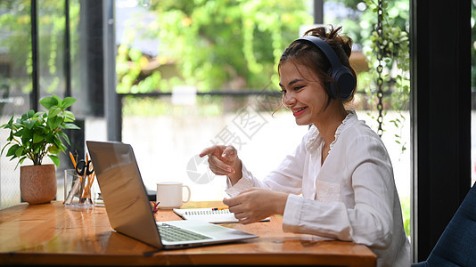 使用笔记本电脑观看网络研讨会视频课程 在学习期间通过笔记本电脑监听讲座的带耳机年轻妇女图片