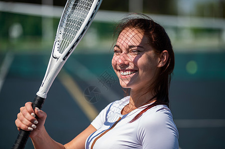 在阳光明媚的一天 美丽的微笑着美丽和笑容的女人 她脸上有网球拍打的影子活力女性黑发球拍训练女士运动服壁球幸福活动图片