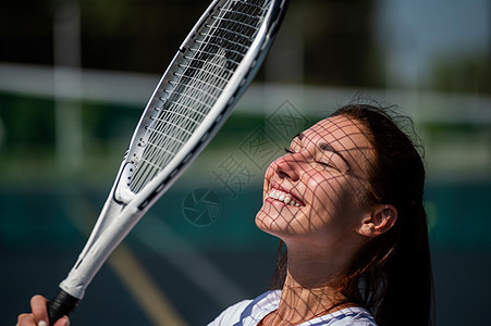 在阳光明媚的一天 美丽的微笑着美丽和笑容的女人 她脸上有网球拍打的影子运动服壁球教练运动竞赛娱乐女士闲暇黑发球拍图片