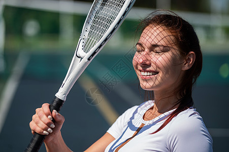 在阳光明媚的一天 美丽的微笑着美丽和笑容的女人 她脸上有网球拍打的影子球拍教练运动服竞赛玩家精力闲暇幸福娱乐运动图片