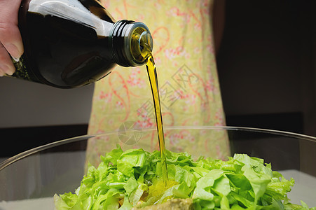 将橄榄油倒入一个玻璃碗中的蔬菜沙拉 女人的手图片