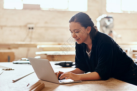 技术在任何地方都占有一席之地 甚至在讲习班中也是如此 一个年轻女性木匠在车间内工作时使用笔记本电脑图片