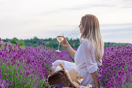 一个女孩在薰衣草田的背景下拿着一杯白葡萄酒 一个女孩在薰衣草田里喝酒紫色横幅玻璃女性女士酒精场地成人农村瓶子图片