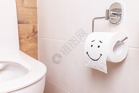 一卷手纸 面带快乐的脸庞 挂在浴室的白墙上洗手间卫生纸腹泻腹痛病痛痔疮地面药品厕纸组织背景图片
