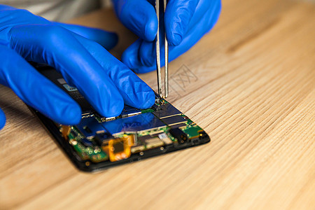修理智能手机主机板的技师 在桌子上的工作间里电路技术男人电气服务焊接技术员硬件母板工具图片