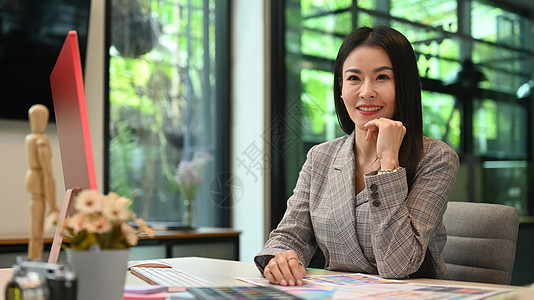 坐在创造性办公室和对镜头微笑的富有创意的亚洲成功的女性创业妇女企业家图片