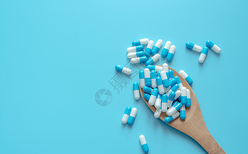 白色药片木勺上的蓝白色胶囊药丸 在蓝色背景的胶囊药片 健康话题 治疗疾病的药物 用药 医疗 医药行业 胶囊丸生产背景