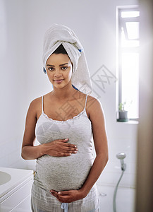 她整个怀孕期间都发光 一个怀孕的年轻女子站在家里的浴室里 被画成肖像图片