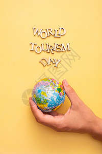 世界旅游日用黄色颜色背景的木纸字母写成文字 女性掌中以全球为顶视图海报海滩铭文创造力游客地球假期旅行运输图片