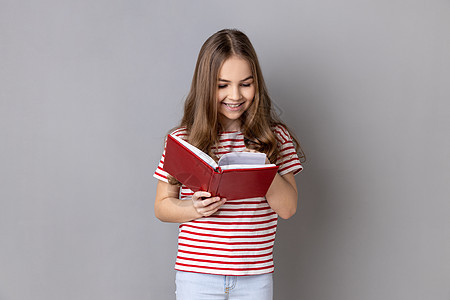 穿条纹T恤的小女孩拿着书 喜欢阅读 站在有趣的情节中生活图片