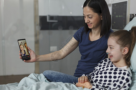 母亲和生病的女儿与最好的朋友在智能手机虚拟视频电话上交谈 (b)图片